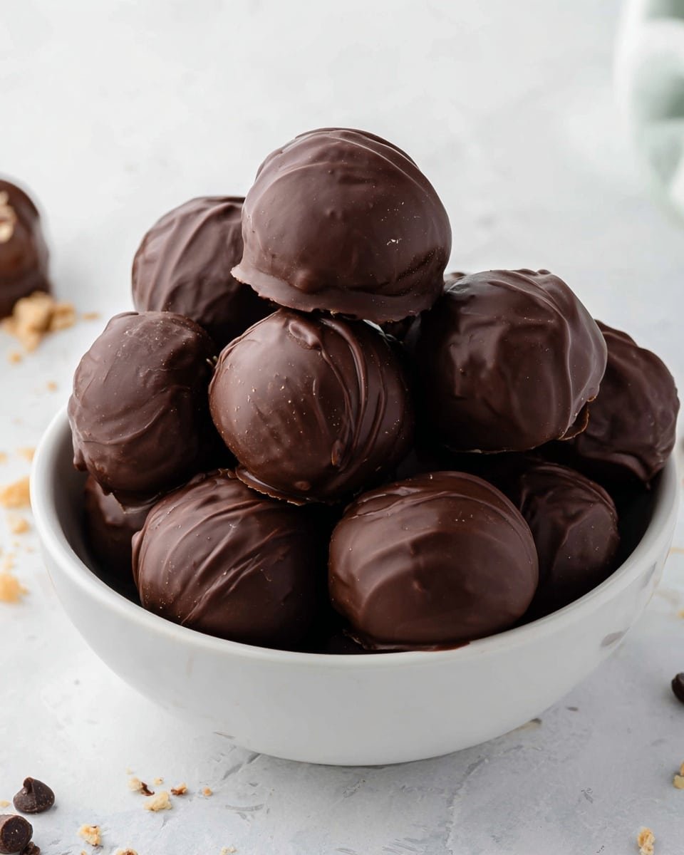A white bowl filled with around ten dark chocolate-covered round truffles with smooth and slightly shiny surfaces, some having small swirls and light wrinkles on the chocolate layer. The truffles are stacked inside the bowl, showing different shapes and slight height variations. The bowl is placed on a white marbled surface with a few small crumbs and chocolate bits scattered around. Soft natural light highlights the textures and rich brown color of the chocolate. photo taken with an iphone --ar 4:5 --v 7