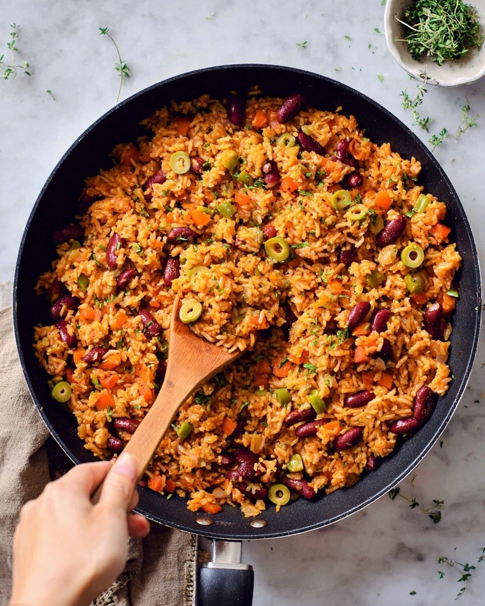 A black frying pan filled with a colorful mix of orange rice, red beans, green olive slices, and small pieces of carrots and herbs. The rice looks soft and mixed well with all the ingredients. A woman's hand is holding a wooden spatula stirring the rice inside the pan. The pan is placed on a white marbled surface with some small green herb leaves scattered around. In the top right corner, there is a white bowl with a bit of green herbs on top. Photo taken with an iphone --ar 4:5 --v 7